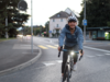 [Translate to Italian:] Junge Frau auf der Strasse mit Velo unterwegs. Sie trägt einen Helm und das Velolicht scheint hell.